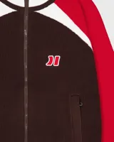 Campera de tejido de punto de grosor medio, con cuerpo marrón oscuro, mangas rojas y detalles en blanco en los hombros, cuello y puños. Presenta cierre frontal y un pequeño logo bordado en el pecho.