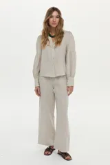 Camisa de lino color beige, con escote en V, cuello mao y mangas abullonadas tres cuartos. Cuenta con cierre frontal de botones y tiras ajustables para atar en la cintura.