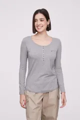 Remera blanca de manga larga, entallada, con cuello redondo y una hilera de botones en el frente. Incluye un pequeño bolsillo decorativo en el pecho.