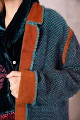 Tapado artesanal tejido en telar con lana teñida, presenta solapas y detalles en cuero natural con terminaciones de pasamanería. Diseño de corte amplio y textura tejida.