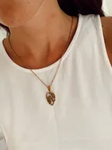 Collar de cadena fina de eslabones con dije colgante en forma de hoja calada, fabricado en acero quirúrgico con acabado dorado.