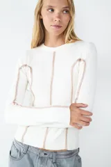 Sweater de manga larga color crudo, confeccionado en tejido de canalé elasticado. Diseño ajustado con cuello redondo y costuras decorativas en contraste color rosado en el frente, la espalda y las mangas.