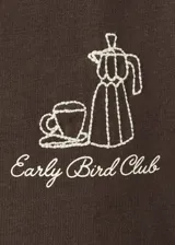 Camiseta marrón de corte recto y mangas cortas, con cuello redondo y pequeño estampado alusivo al café en el pecho.