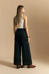 Jean de corte wide leg y tiro alto, color negro con costuras en contraste color ocre. Presenta bolsillos delanteros y traseros con detalle de pespunte, y ruedo ancho con costura decorativa.
