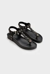 Sandalia baja de cuero vacuno color negro, tipo thong sandal, con tira vertical en el empeine decorada con apliques metálicos en forma de flores y tira ajustable en el talón con hebilla.