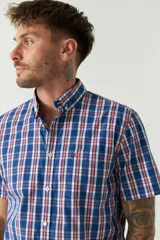 Camisa de manga corta con estampado de cuadros vichy en azul y blanco. Presenta cuello con botones, cierre frontal con botones y logo bordado en el pecho.