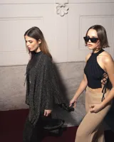 Ruana o poncho de tejido de punto negro con hilos dorados brillantes, de corte amplio y mangas largas.