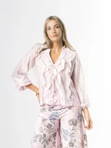 Camisa de organdí rosa pastel con finas rayas verticales metalizadas, escote en V con volados frontales y mangas largas abullonadas con puños elásticos.