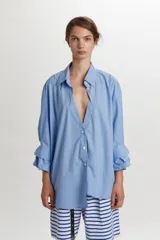 Camisa azul celeste de algodón, con corte oversize y diseño asimétrico en el ruedo. Cuenta con cuello camisero, cierre frontal con botones y mangas largas con puños estructurados y detalle fruncido.