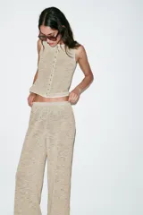 Top tipo chaleco de tejido de punto con algodón, color beige con detalles texturizados. Presenta cuello redondo, sin mangas y cierre frontal con una hilera de botones.