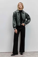 Cazadora de estilo bomber confeccionada en material efecto piel color verde oscuro. Presenta cuello camisero, cierre frontal con cremallera, mangas largas abullonadas con puños elásticos y un corte ligeramente cropped.