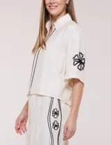 Conjunto de dos piezas negro compuesto por camisa de manga corta con cuello camisero y pantalón palazzo de tiro alto. Presenta detalles de bordados florales en contraste a lo largo de los laterales del pantalón y en las mangas.