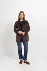 Chaqueta de gamuza color tostado con cuello camisero, cierre frontal de botones y bolsillos delanteros con solapa.