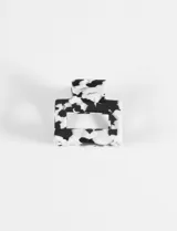 Broche de pelo tipo pinza de forma rectangular con calado central, confeccionado en acrílico con diseño jaspeado en blanco y negro.
