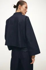Pantalón de tiro alto confeccionado en denim oscuro, con pinzas delanteras que aportan volumen y pernera abullonada. Cuenta con bolsillos frontales, falsos bolsillos traseros con solapa y bajo ajustable mediante botones a presión.