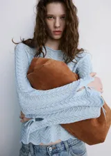 Buzo de punto celeste con diseño recto, detalles calados, cuello redondo y manga larga con cordones ajustables en los puños.