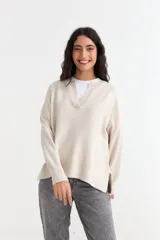 Sweater de tejido de punto color beige, con cuello abierto tipo polo, mangas largas y tajos laterales en el ruedo.