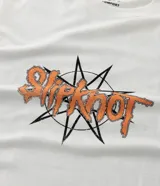 Remera blanca de algodón con cuello redondo y mangas cortas. Presenta un estampado grande en la espalda con un collage de nueve máscaras de los miembros de la banda Slipknot, con texto en la parte inferior.