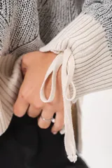 Buzo tejido de punto bicolor en tonos crudo y gris, con silueta relajada, mangas amplias con jaretas regulables en los puños y cuello redondo.