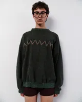 Sweater tejido de lana color verde oscuro con bordado manual en forma de zigzag en tonos blanco, naranja y marrón. Tiene cuello redondo y terminaciones acanaladas en puños y ruedo.