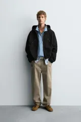 Cazadora negra de algodón con efecto lavado, corte relajado y capucha ajustable. Presenta cierre frontal de cremallera, bolsillos frontales tipo canguro y elásticos en puños y bajo.