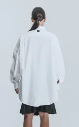 Camisa blanca de manga larga, confeccionada en poplín de algodón, con calce oversize y un bolsillo frontal asimétrico y poco convencional.