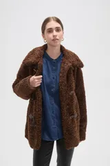 Campera de textura tipo corderito en color marrón, con cuello solapa y cierre frontal mediante tres botones tipo duffle con presillas de cuero sintético.