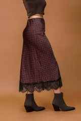 Falda midi de seda con estampado de lunares rojos sobre fondo oscuro, con detalle de encaje negro en el ruedo.