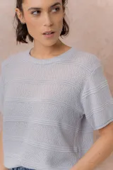 Sweater tejido celeste de manga corta con textura y delicadas líneas horizontales en relieve. Presenta cuello redondo y calce amplio con hombros caídos.