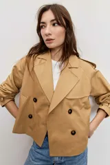 Cazadora corta de estilo gabardina en color tostado, con diseño cruzado de doble botonadura, solapas amplias, mangas largas con trabillas en los puños y hombreras.