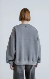 Buzo de cuello redondo con diseño oversize y corte crop. Confeccionado en frisa de algodón color gris melange, presenta un recorte asimétrico en color negro en microfibra con un bolsillo frontal funcional con cierre a presión.