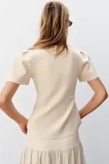 Chaqueta entallada azul marino de punto, con cuello redondo y mangas cortas abullonadas con aberturas. Cierre frontal con botones forrados a tono.