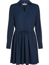 Vestido corto camisero azul marino de Tommy Hilfiger, con cuello italiano, mangas largas con puños abotonados, cinturón anudable en la cintura y logo metálico en el bajo.