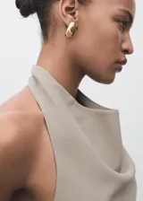 Top color beige, con cuello drapeado, diseño sin mangas, espalda abierta con cierre de lazo y dobladillo asimétrico.