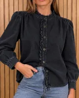 Camisa de denim negra con detalles de volados sutiles en el cuello alto y a lo largo de la botonera frontal. Posee frunces en los hombros y mangas largas abullonadas con puños ajustados.