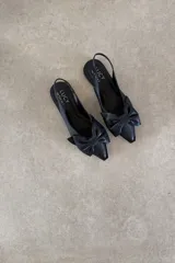 Zapato chatita destalonada de cuero negro, con punta fina y detalle de moño grande en el empeine.