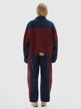 Campera tipo trucker de corte oversize, confeccionada en algodón con diseño colorblock en tonos azul marino y bordó. Presenta cierre frontal con botones metálicos, cuello clásico y bolsillos frontales con solapa.