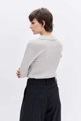 Jersey de punto color beige con cuello polo y cierre frontal de botones. Presenta mangas largas y un ajuste entallado al cuerpo.