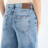 Pantalón jean de tiro bajo, color azul con lavado medio, corte ancho y recto, con cordón ajustable en la cintura.