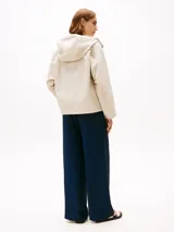 Campera beige de Tommy Hilfiger, con capucha con cordón ajustable y cierre frontal con cremallera y botones a presión. Tiene dos bolsillos delanteros tipo sobre con botón y logo metálico de Tommy Hilfiger en el puño.