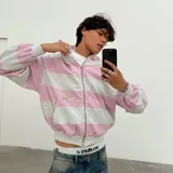 Campera con capucha de corte boxy, con diseño de rayas horizontales en tonos gris melange y rosado. Presenta la inscripción bordada en relieve de la marca en la espalda en tono amarillo pastel.