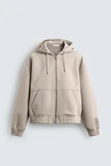 Sudadera tipo hoodie con cierre frontal de cremallera, confeccionada en tejido técnico de algodón con efecto neopreno. Presenta un corte relajado, capucha ajustable con cordones, bolsillos frontales tipo canguro y terminaciones con elástico en puños y ruedo.