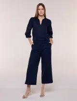 Pantalón crop de lino y algodón color blanco, con calce holgado, pierna ancha de corte recto y cintura elástica. Presenta bolsillos laterales y detalle de puntilla aplicada en el frente.