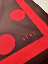 Pañuelo cuadrado de tela con estampado de lunares rojos sobre fondo marrón, con borde en contraste.