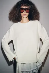 Camiseta color crudo de cuello redondo y manga larga, con detalle de aplicación de tejido lencero asimétrico a tono en el ruedo.