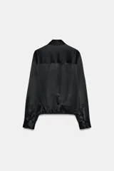 Camisa de satén con cuello solapa, manga larga con puños y bajo ajustable mediante cordones. Presenta cierre frontal con botones ocultos.