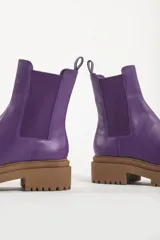 Bota tipo chelsea con suela track de goma en color marrón y capellada de cuero negro. Presenta elásticos laterales y tirador trasero.