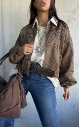 Campera tipo bomber de gamuza color marrón, con diseño bordado de motivos florales en toda la prenda. Presenta cierre frontal, cuello redondo y mangas largas con puños elásticos.