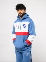 Canguro con capucha de Umbro del Club Nacional de Football, con diseño de bloques de color en azul, blanco y rojo. Presenta bolsillo frontal tipo canguro, cordones ajustables en la capucha y logos bordados del club y la marca.