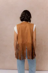 Chaleco de gamuza sintética color tostado, con diseño abierto sin cierre. Presenta bordados decorativos en hilo blanco y flecos largos en el delantero y la espalda.